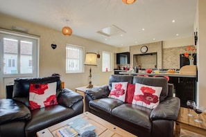A living room with a sofa set, a coffee table, and a kitchen area in the background. - 1 Bed in Blofield Heath (oc-1466) (Blofield)
