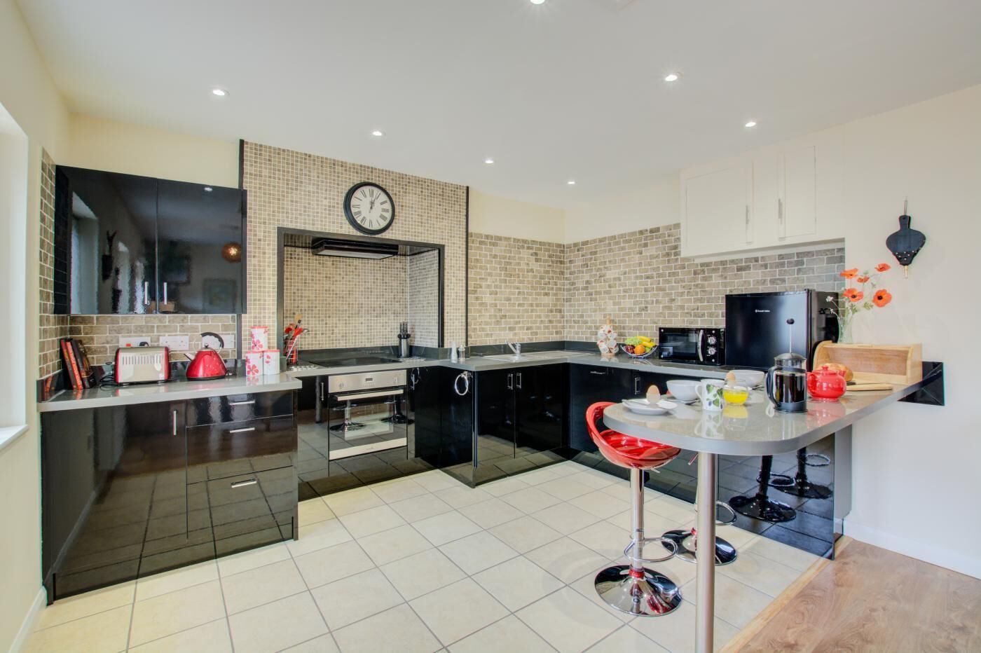 A modern kitchen with a central island, black cabinets, a microwave, and a clock on the wall.