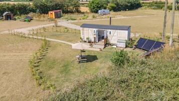 A small house with a porch, a solar panel, and a trailer in a rural setting.