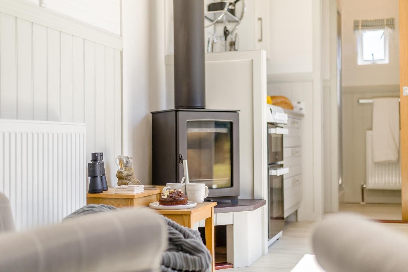 A cozy living room with a fireplace, a coffee table with a cake, and a view into the kitchen.