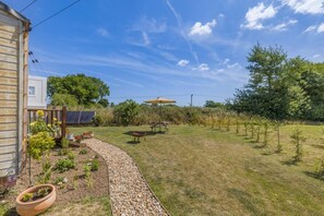 Un jardin avec une terrasse en bois, un espace barbecue et un potager où diverses plantes sont cultivées.