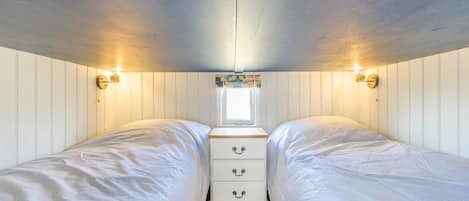 Una habitación con dos camas, una ventana pequeña y luces fijadas a la pared.