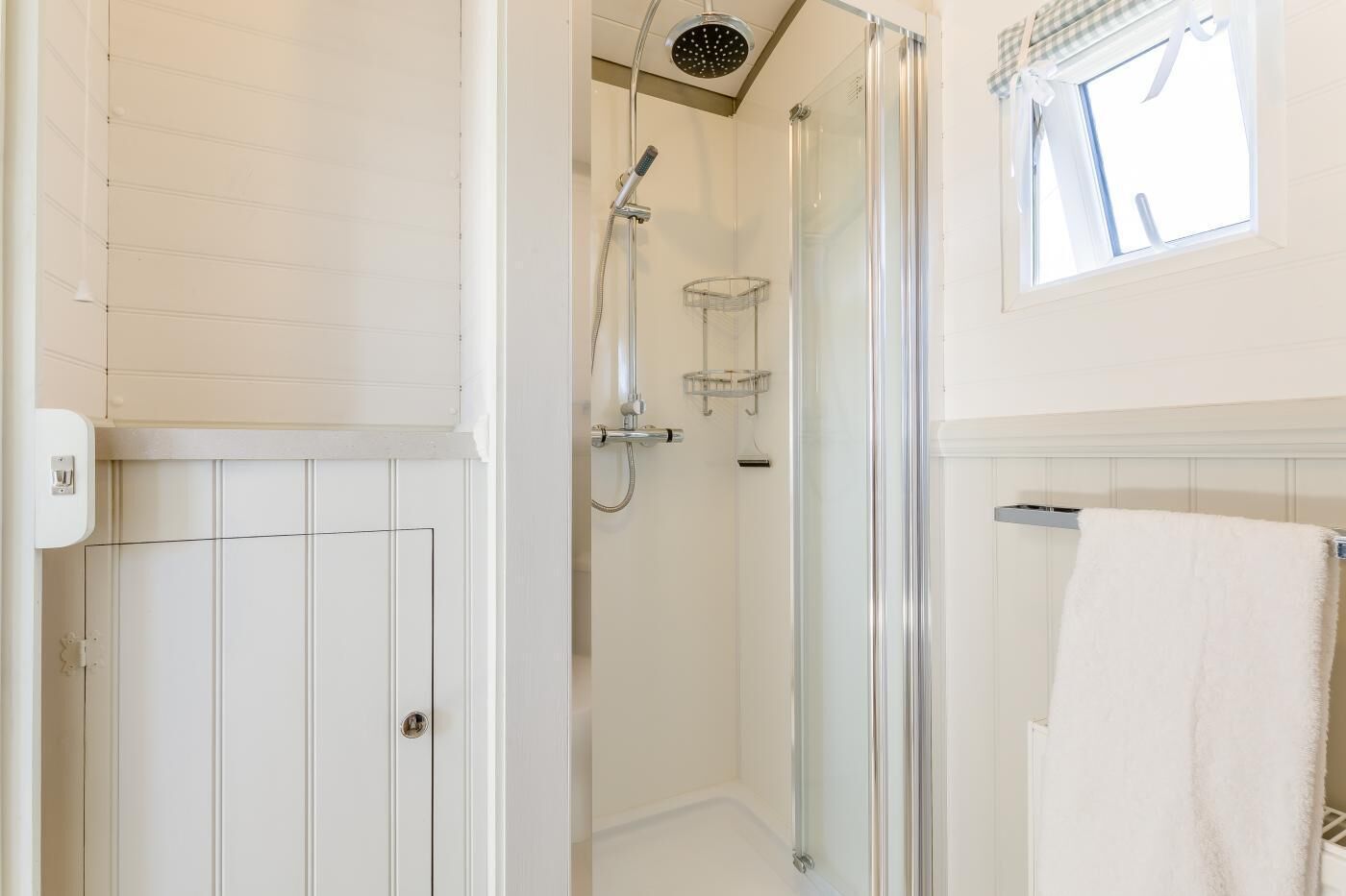 A modern bathroom with a glass-enclosed shower, a towel rack, and a window with curtains.