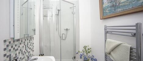 A bathroom with a glass shower enclosure, a white sink, a towel rack with a towel, and a painting on the wall.