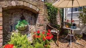 A brick wall with a decorative stone shelf, a chair, a table with a white umbrella, and red flowers. - 2 Bed in Rye (oc-rh1045) (Rye)