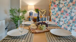 A dining table set with plates, glasses, a bottle, and a centerpiece of grapes and cheese. - 2 Bed in Broadstairs (oc-th017) (Broadstairs)