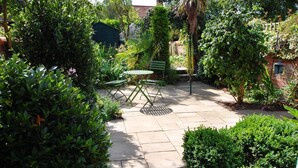 Un espace patio avec une table et des chaises vertes, entouré d’une végétation luxuriante et d’un mur de briques.