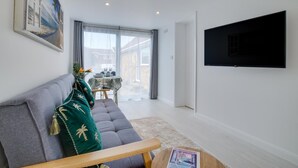 A modern living room with a grey sofa, a flat-screen TV mounted on the wall, and a dining area with a table and chairs. - 1 Bed in Saltdean (oc-bbidre) (Saltdean)