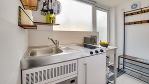 A compact kitchen with a sink, stove, and toaster. There is a window above the sink, and a shelf with kitchen utensils. - 1 Bed in Saltdean (oc-bbidre) (Saltdean)
