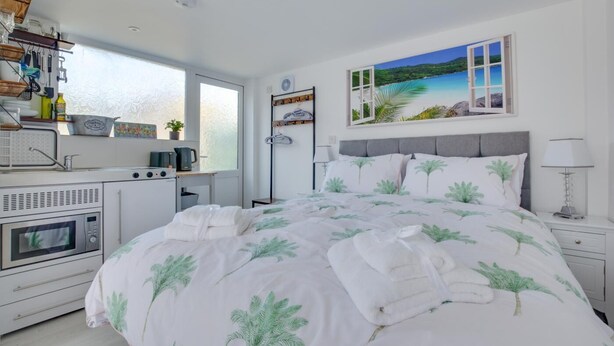 A bedroom with a bed, a small kitchenette, a window with a view, and a painting on the wall. - 1 Bed in Saltdean (oc-bbidre) (Saltdean)