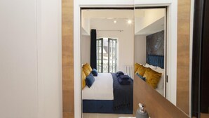 A modern bedroom with a large bed, a bathroom with a sink, and a view of the outdoors through a large window. - 2 Bed in Bath (oc-bhr8) (Bath)