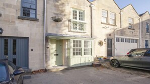 A two-story stone building with a green door, a small window with a decorative grille, and a white garage door. - 2 Bed in Bath (oc-bhr8) (Bath)