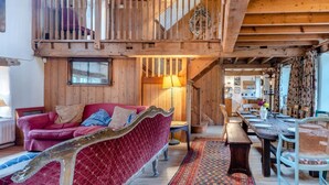Ein geräumiges Loft mit hoher Decke, Holzbalken, einem roten Sofa, einer Essecke mit einem langen Tisch und einer Treppe, die zu einer oberen Ebene führt.