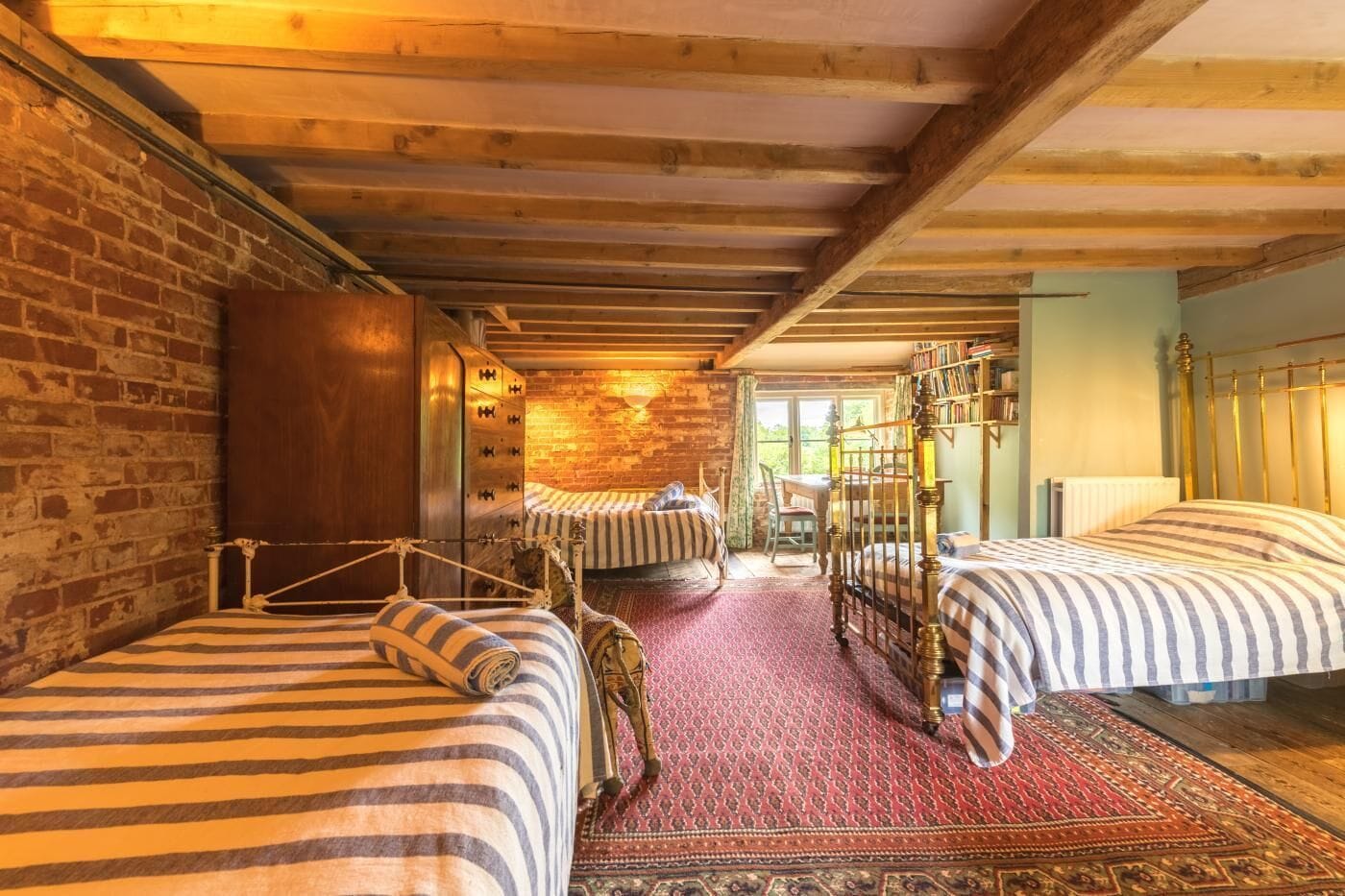A rustic room with three beds, a brick wall, and a wooden ceiling.