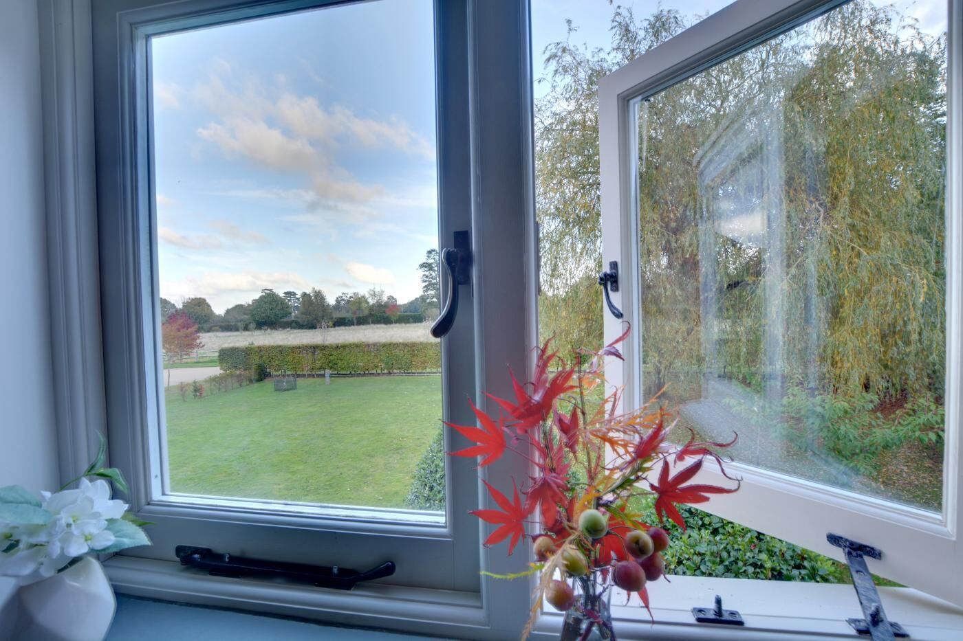 A window with a view of a grassy area and trees, a vase with flowers, and a door handle.