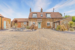 A stone house with a tiled roof, a gravel driveway, and a small garden with plants. - 4 Bed in Ringstead (oc-1672) (Ringstead)