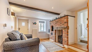 A modern living room with a fireplace, a sofa, and a view of the street. - 4 Bed in Ringstead (oc-1672) (Ringstead)