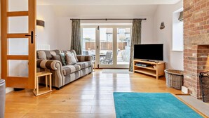 A living room with a sofa, TV, and a view to the outside. - 4 Bed in Ringstead (oc-1672) (Ringstead)