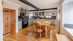 A modern kitchen with a dining area, featuring a wooden table and chairs, a built-in oven, and a large window providing natural light. - 4 Bed in Ringstead (oc-1672) (Ringstead)