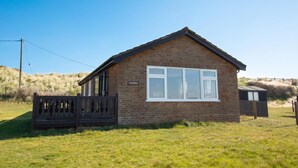A small brick building with a sign reading "Happidays." It has a pitched roof, large windows, and a wooden fence in front. - 3 Bed in Eccles Beach (oc-852) (Eccles-on-Sea)