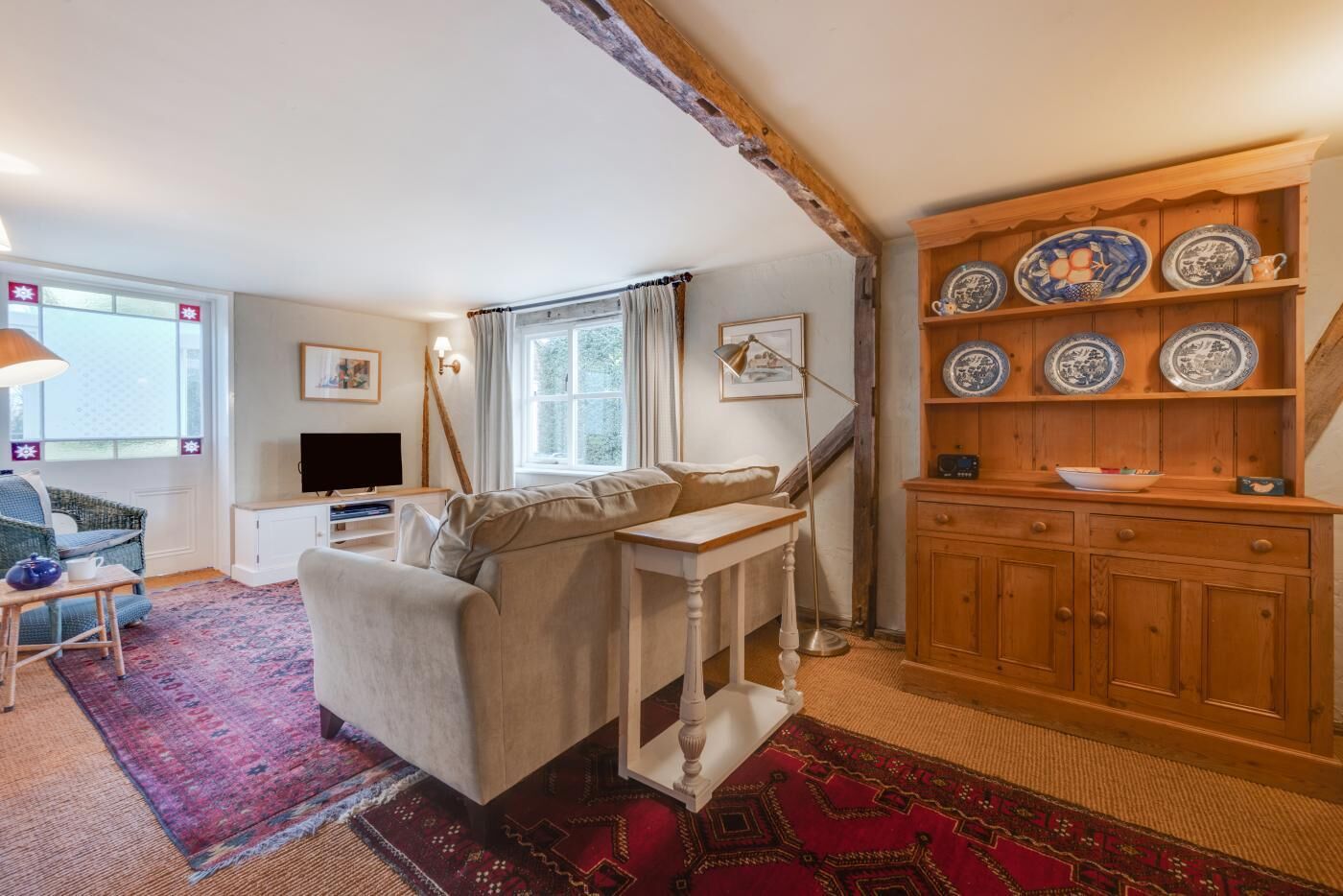 A cozy living room with a sofa, a small table, a TV, and a wooden cabinet with decorative plates.