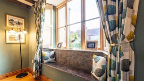 A cozy room with a built-in bench by a large window, framed pictures, and a floor lamp. - 4 Bed in Roughton (oc-1435) (Roughton)