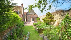 A stone house with a tiled roof, a small garden with a pathway, and a brick wall. - 4 Bed in Roughton (oc-1435) (Roughton)