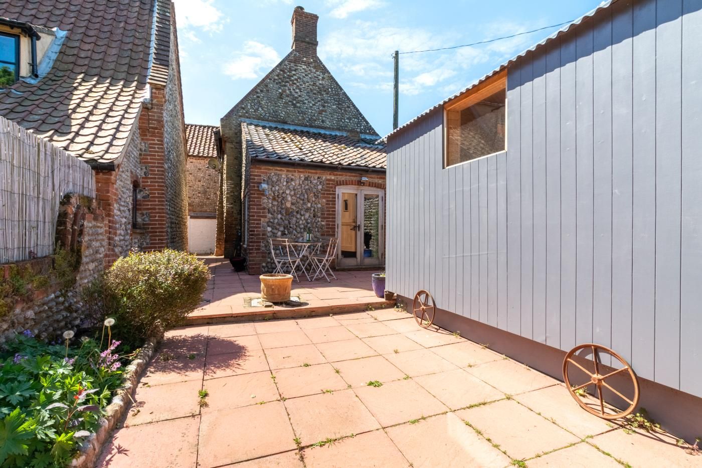 A courtyard with a tiled patio, a brick building, a white wooden structure, and a small garden area.