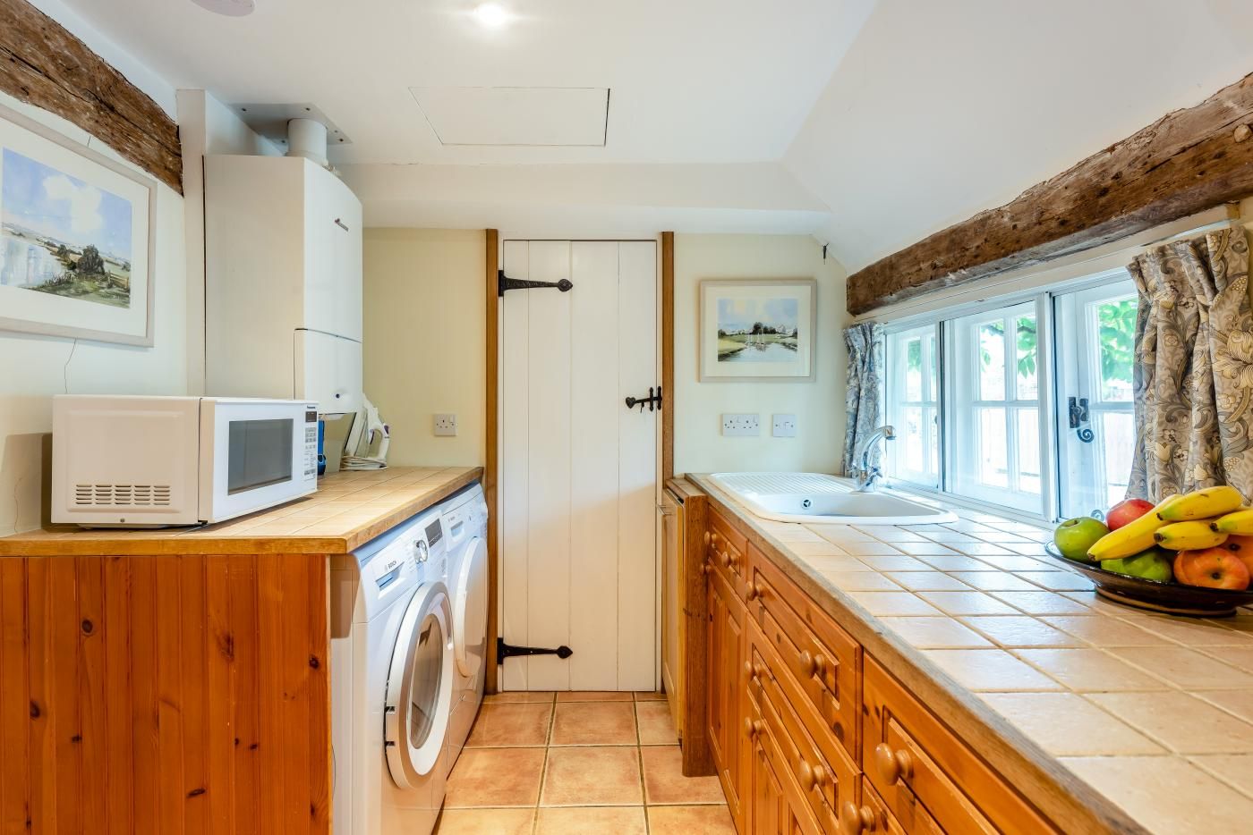 A compact kitchen with a washing machine, microwave, and a sink with a fruit bowl.