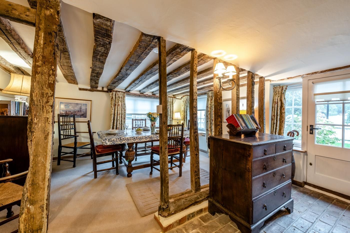 A rustic interior with exposed wooden beams, a dining area with a table and chairs, and a wooden dresser with drawers.