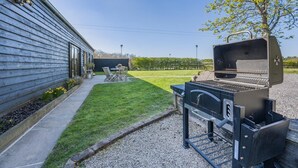 A backyard with a barbecue grill, a patio table, and chairs. - 3 Bed in Staplecross (oc-rh1162) (Sedlescombe)