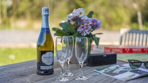 A bottle of Prosecco wine, two empty wine glasses, a bouquet of flowers, and a book on a wooden table. - 3 Bed in Staplecross (oc-rh1162) (Sedlescombe)