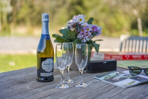 Eine Prosecco-Flasche, zwei leere Weingläser, ein Blumenstrauß und ein Buch auf einem Holztisch.
