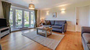 A living room with a sofa, a coffee table, a TV, and a sliding glass door leading to an outdoor area. - 3 Bed in Staplecross (oc-rh1162) (Sedlescombe)