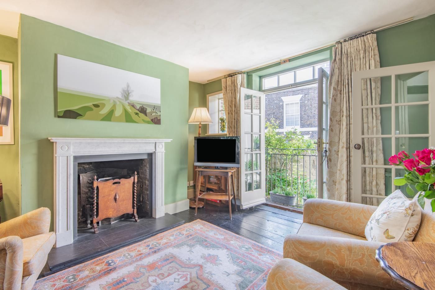 A living room with a fireplace, a television on a wooden stand, a patterned rug, and a sofa with a decorative pillow.