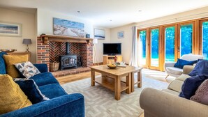 A cozy living room with a brick fireplace, a television, and a dining table. - 3 Bed in Fakenham (oc-1315) (Thursford)
