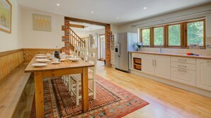 A spacious kitchen with wooden flooring, a dining area with a long table, and a built-in brick fireplace. - 3 Bed in Fakenham (oc-1315) (Thursford)