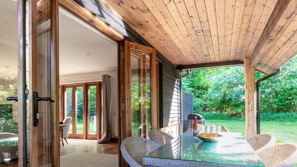 A covered outdoor dining area with a glass table and wicker chairs, connected to an indoor space with a sliding glass door. - 3 Bed in Fakenham (oc-1315) (Thursford)