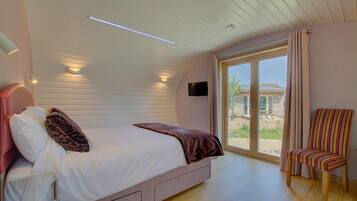 A bedroom with a bed, a chair, a TV, and a sliding glass door to the outside.