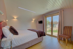 A bedroom with a bed, a chair, a TV, and a sliding glass door to the outside.