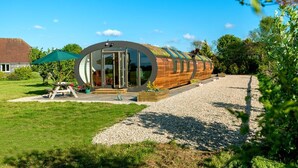 A modern, curved wooden building with large glass doors, a gravel driveway, and a picnic table with a green umbrella.