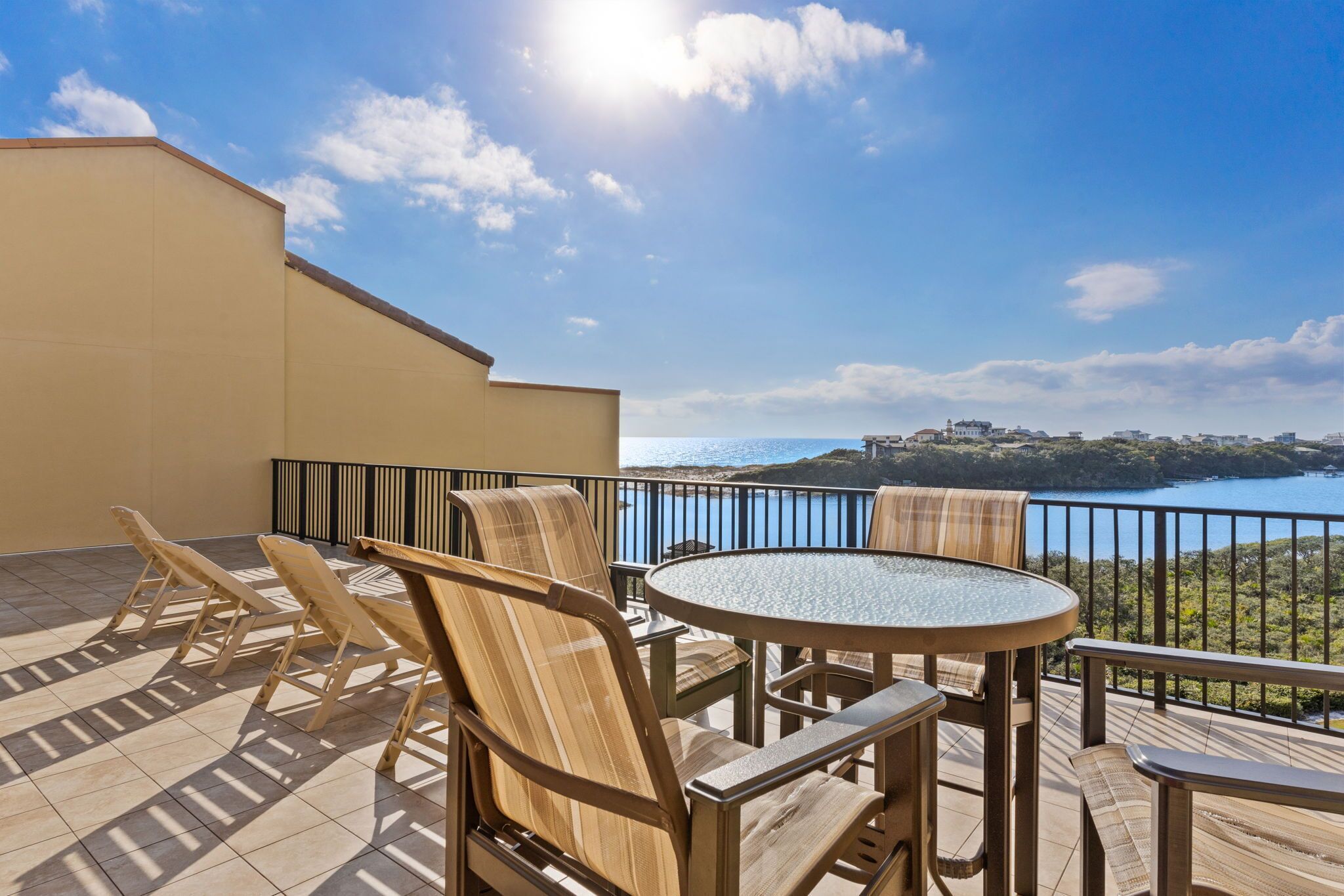 A terrace with a round table and chairs, overlooking a body of water and a distant town.