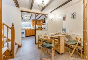 Una cuina acollidora amb armaris de fusta, una taula de dinar amb cadires i una vista cap a la sala de estar adjacent.