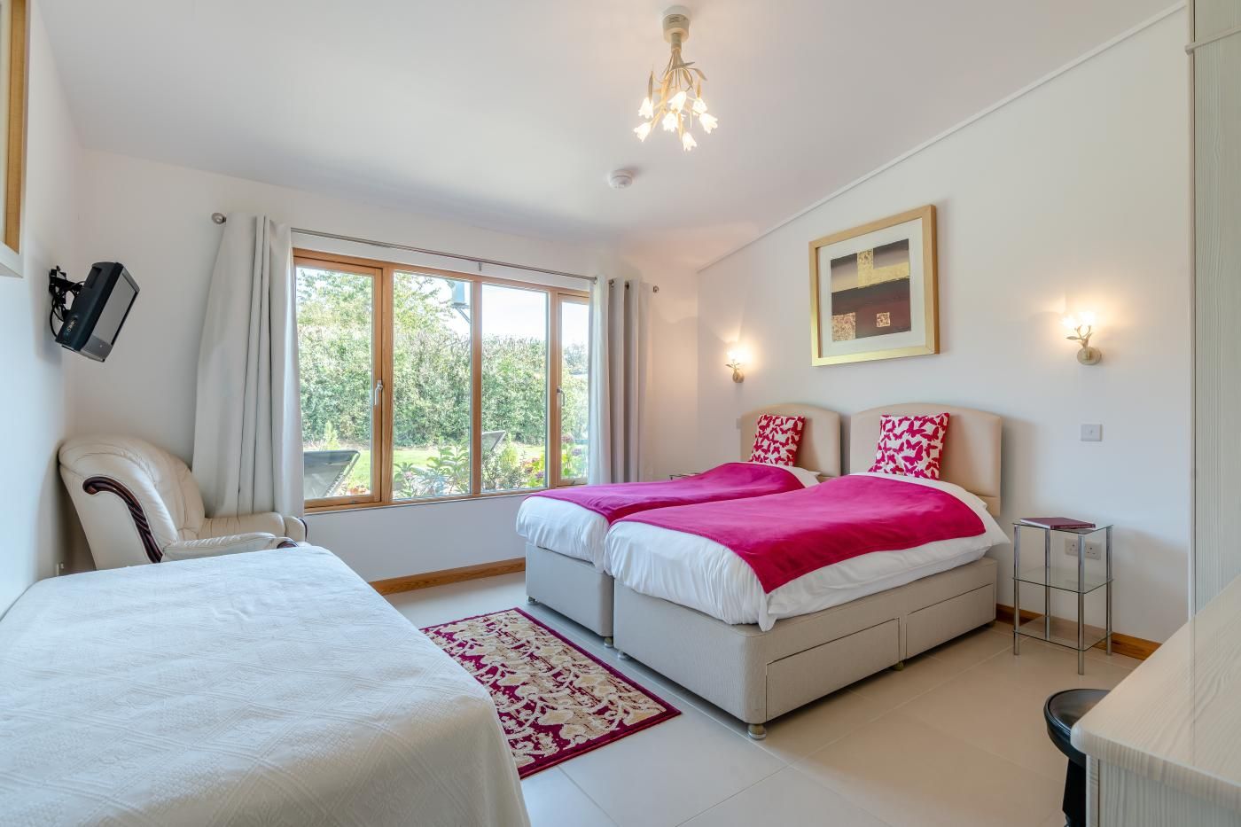 A bedroom with two beds, a chair, a desk, and a large window.