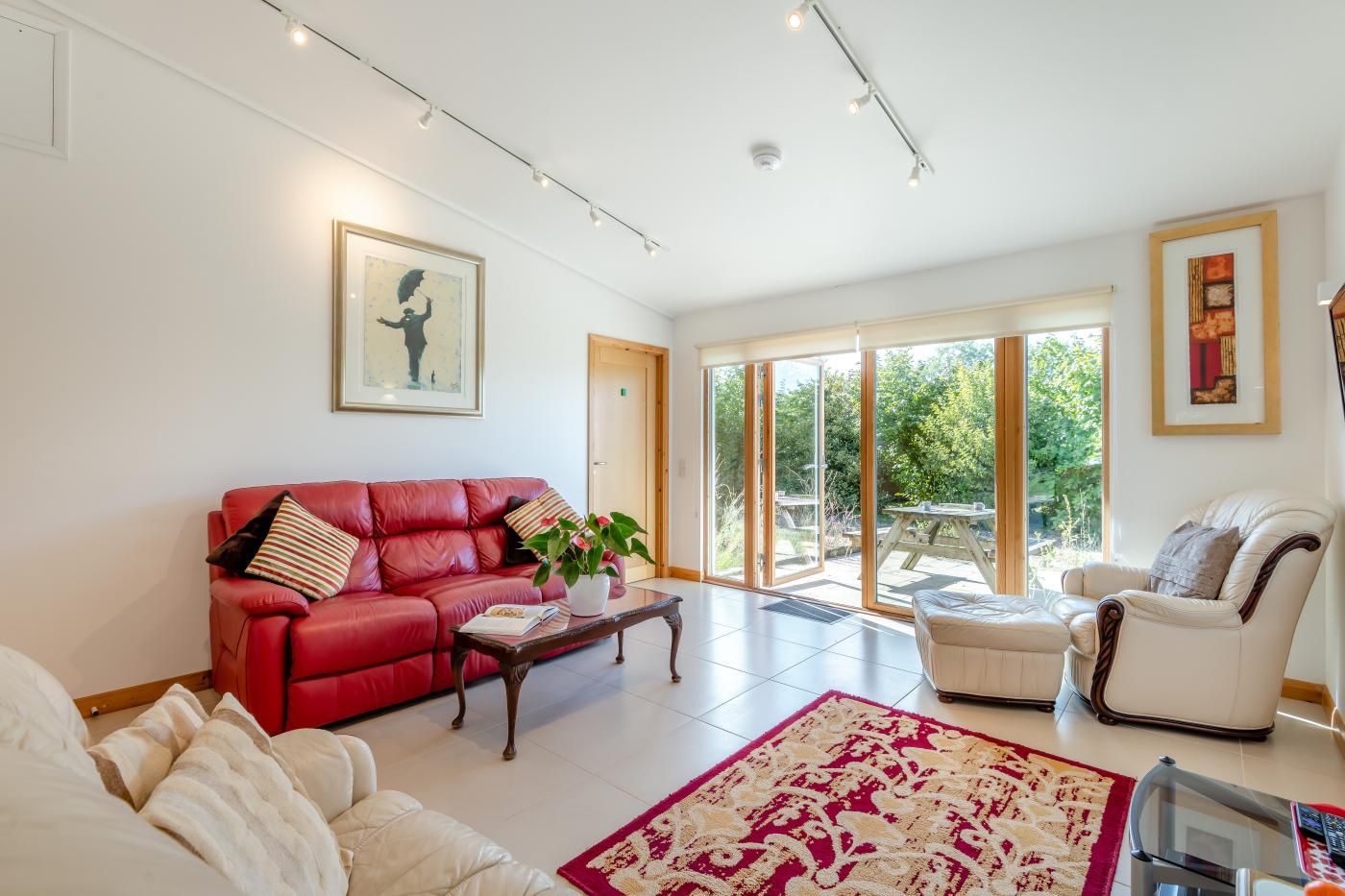 Un salon spacieux avec un canapé en cuir rouge, un fauteuil blanc et une table basse. Une grande fenêtre offre une vue sur la verdure environnante.