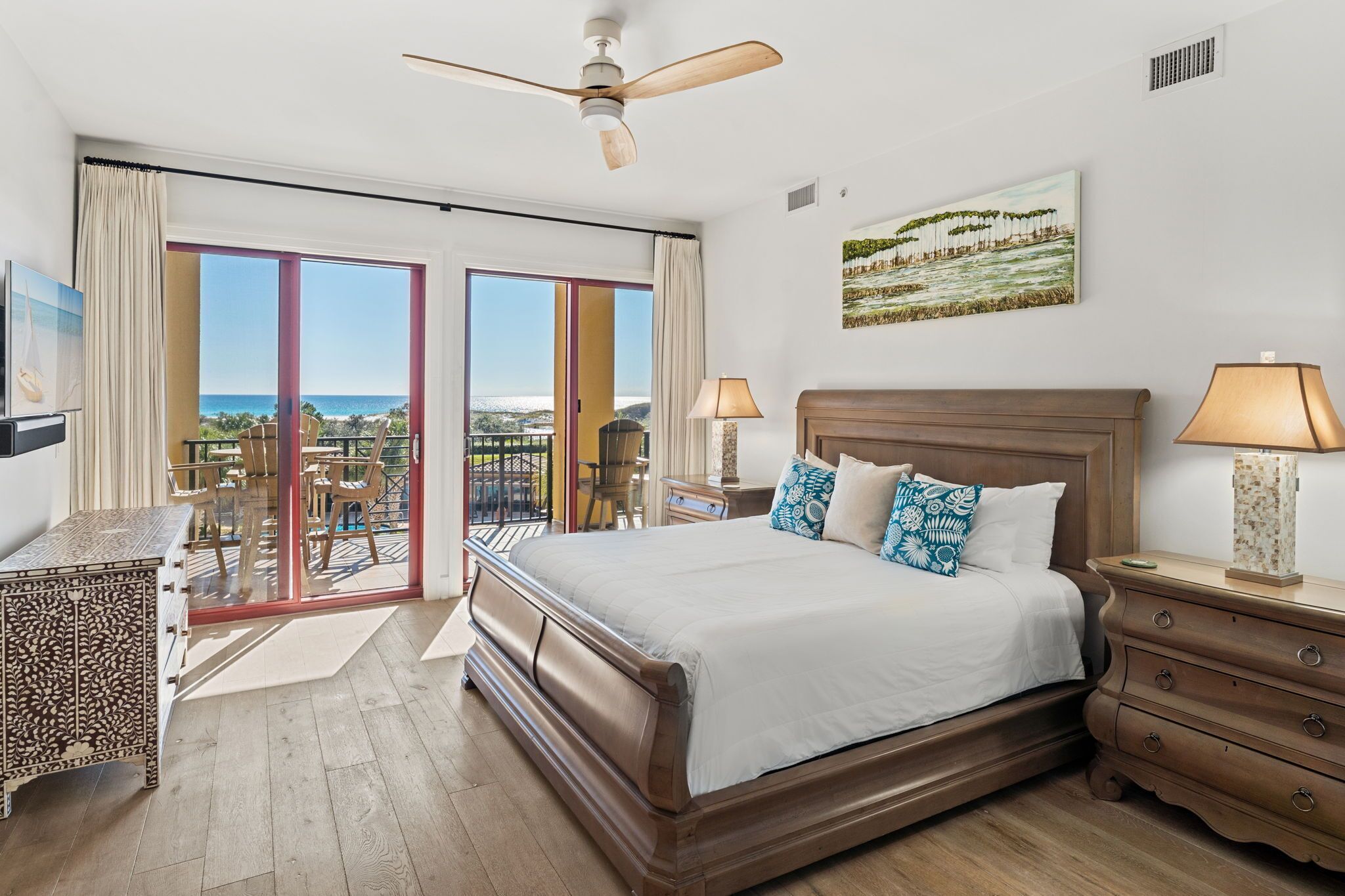 Ein Schlafzimmer mit einem großen Bett, einem Deckenventilator, einem Nachttisch, einer Kommode und einem Balkon mit Meerblick.