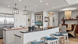 A modern kitchen with white cabinetry, a central island with bar stools, and a dining area with a chandelier. - Wonderful Condo on 30A! (Santa Rosa Beach)