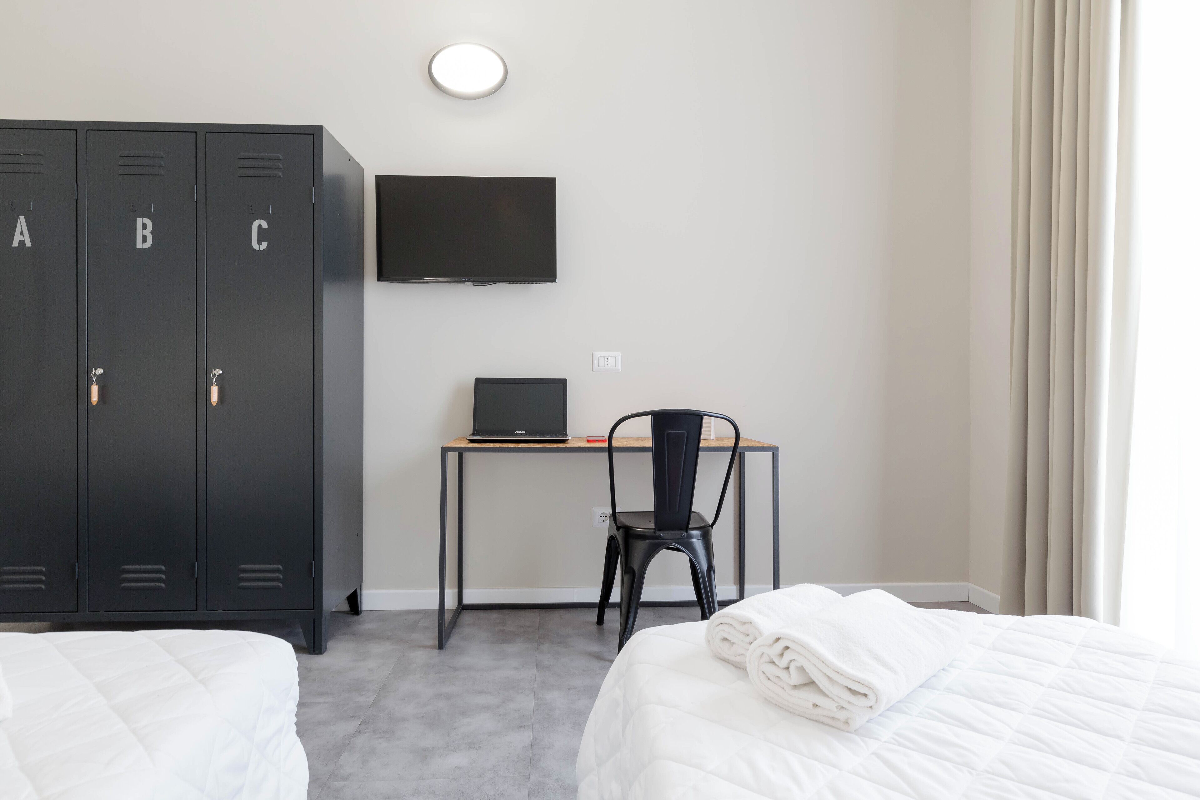 Ett hotellrum med två sängar, ett skrivbord med en bärbar dator, en stol och en tv på väggen.