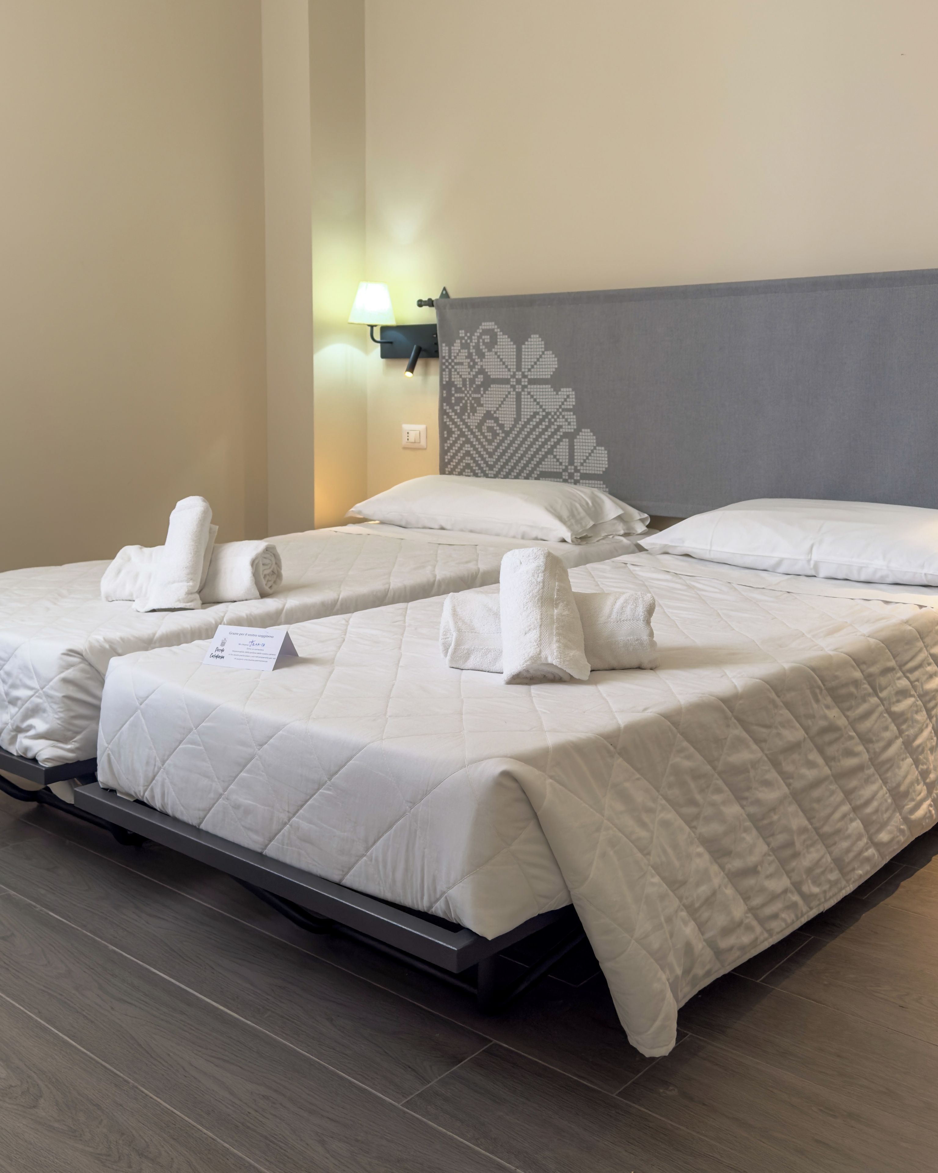 Una habitación de hotel con dos camas, cada una con una colcha blanca acolchada y toallas bien dobladas.