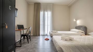 Una habitación de hotel con escritorio, dos camas, armario y un ventanal con cortinas.